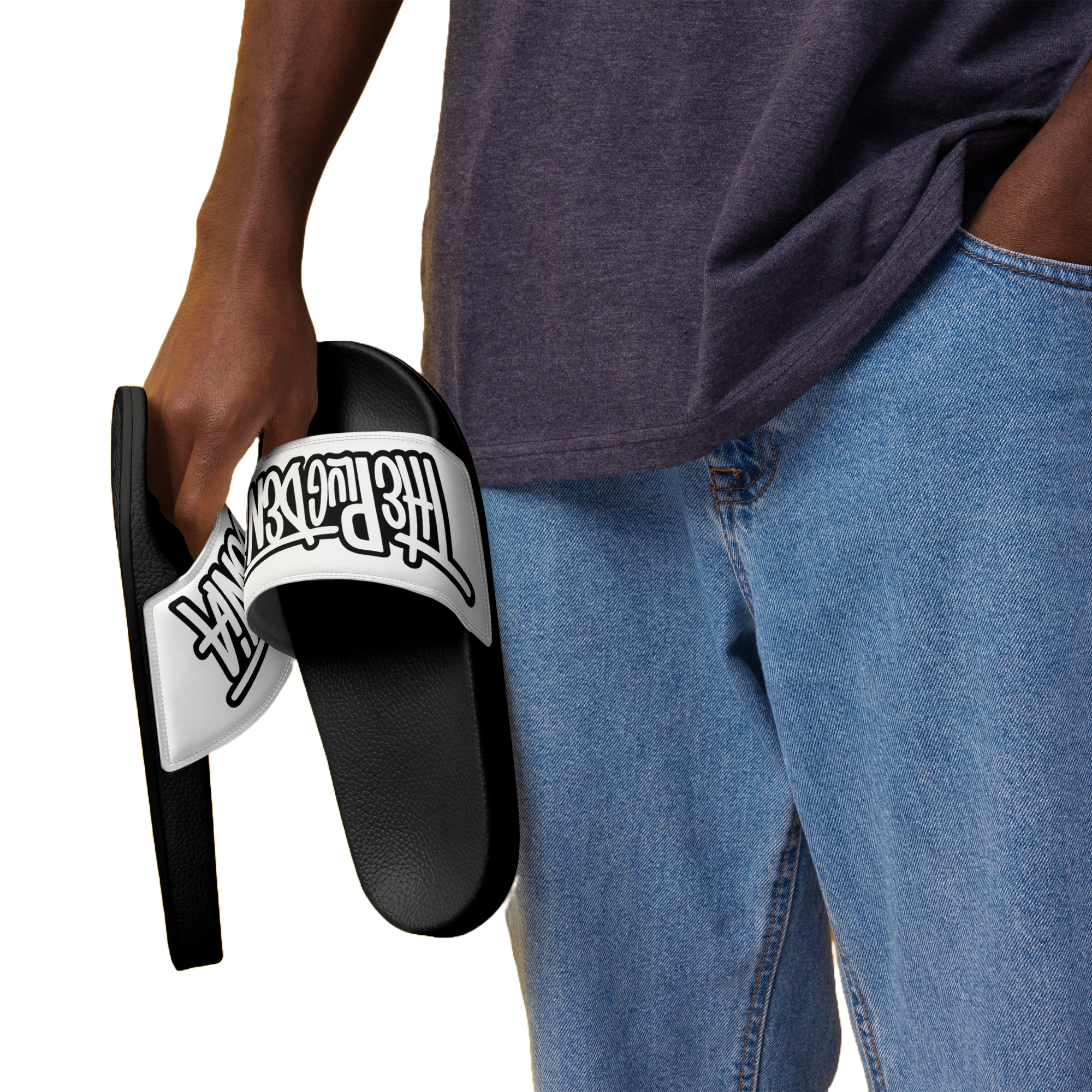 A person wearing a dark gray t-shirt and blue jeans holds a black slide sandal with a white strap featuring the 'The Powerpuff Girls' logo in black.